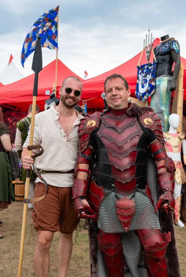 Two guests, one in red dragon-scale armour, beside a merchant tent